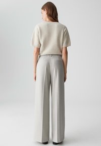 Un pull en crème léger à texture, à manches courtes, associé à un pantalon ample à taille haute de couleur gris clair avec des poches arrière.