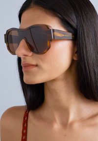 Occhiali da sole oversize tartarugati con lenti scure e montatura spessa, caratterizzati da angoli netti e una finitura lucida.
