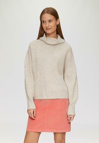 Beige gebreide trui met een colhals en geribbelde textuur, gecombineerd met een roze corduroy mini rok. Eenvoudig, ontspannen model.