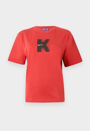 T-shirt vermelha de algodão com design gráfico preto em forma de 'K' e riscas num remendo quadrado. Mangas curtas e decote redondo.