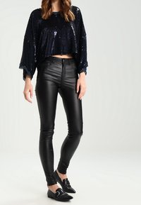 Laivastonsiniset paljettiyksityiskohtaiset lyhyt paita leveillä hihoilla, yhdistetty mustiin istuviin nahkahousuihin ja mustiin loafereihin. Sileät tekstuurit ja kiiltävät yksityiskohdat.