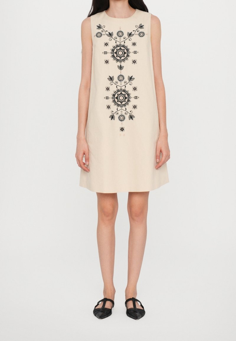 Vestido sin mangas beige con bordado floral negro en un diseño simétrico. Longitud por encima de la rodilla, corte relajado y textura suave.