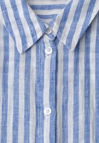 Chemise en lin rayée verticalement bleu et blanc à l'avant avec col et trois boutons blancs fermés.