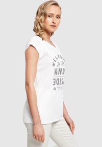 Hvid bomulds-t-shirt med et gr�åt grafisk print, der står "VELKOMMEN TIL DEN OMVENDTE VERDEN", korte ærmer og en afslappet pasform.