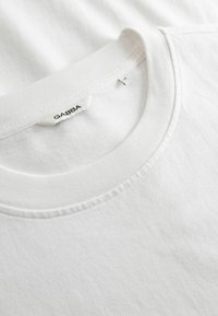 Witte T-shirt met ronde hals en zichtbaar merkembleem "GABBA" en maatlabel in de kraag, op een gladde stoffen achtergrond.