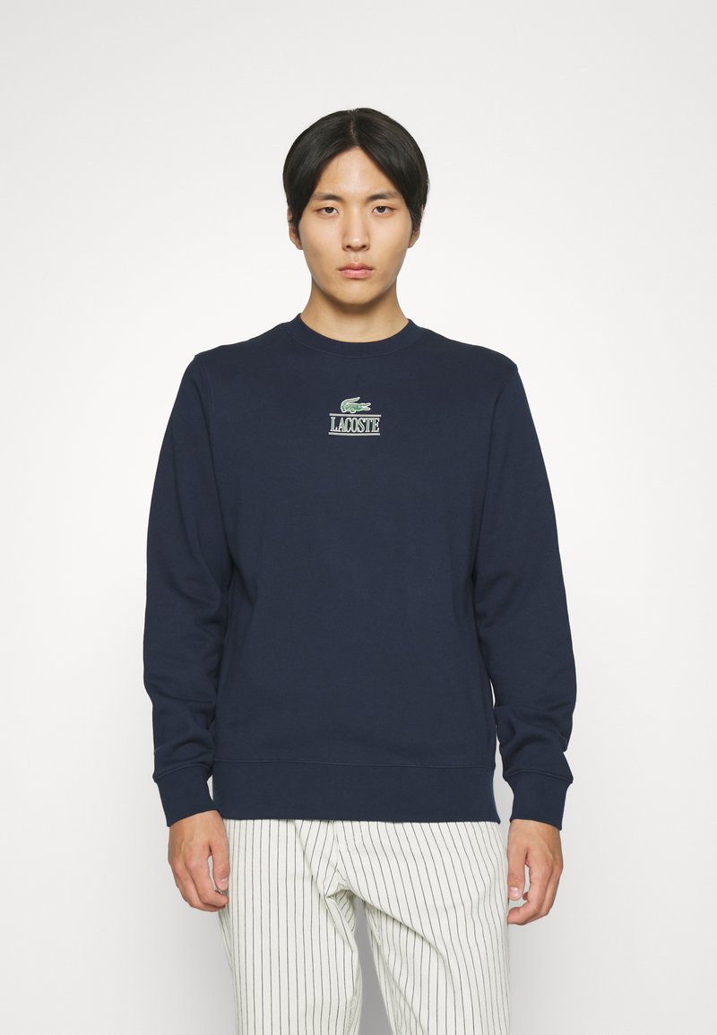 Granatowy sweter z bawełny z elastycznymi mankietami i dołem, z zielono-białym logo Lacoste na piersi.