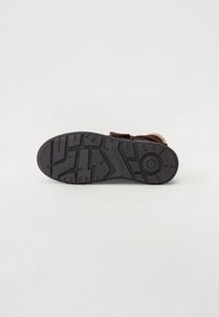 Semelle de chaussure en caoutchouc texturé marron avec un motif de traction détaillé et un emblème circulaire, muni d'un bord supérieur doux et rembourré.