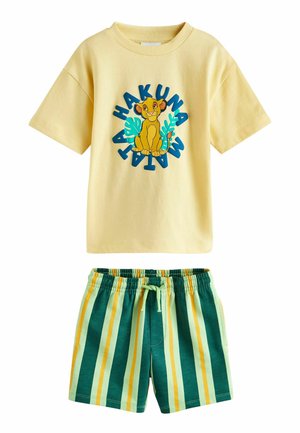 Geltona trumpomis rankovėmis marškinėliai su Simba ir tekstu „Hakuna Matata“, derinami su žaliais, geltonais ir šviesiai mėlynais dryžuotais elastiniais šortais.