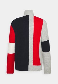 Stickad tröja med hög krage som har djärva rutor i röd, marinblå och grå. Mjuk textur med kontrasterande ränder och en färgblockerad design.