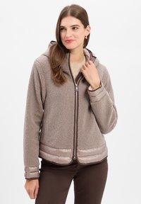 Fleece-lined hooded jacket in taupe with a zip front. Features a smooth, satin-like hem and cuffs. Textured exterior with a cozy appearance.
