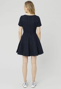 Robe évasée bleu marine à manches courtes, en tissu texturé avec des éclats dorés, col rond et corsage ajusté. Portée avec des baskets blanches.