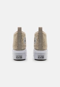Baskets montantes beiges à texture duveteuse avec une semelle en caoutchouc blanche. Dotées d'un patch logo et d'une tirette arrière beige pour un enfilage facile.