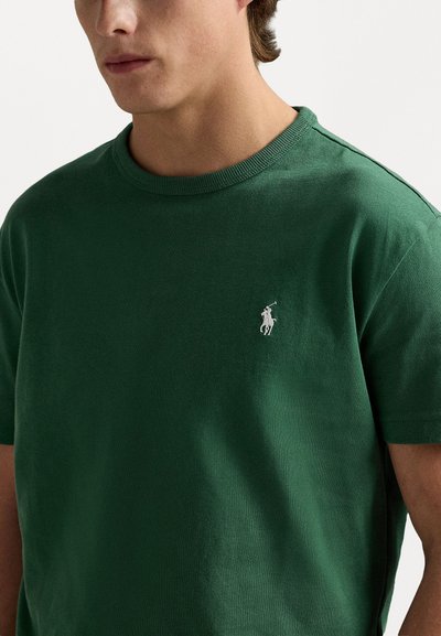 Grön bomullströja med rund halsringning, korta ärmar och en liten vit polo-logotyp på vänster bröst. Mjuk, slät textur.