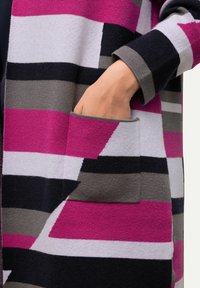 Randig kofta i rosa, grå och svart. Har en ficka med lappar och ett mjukt, strukturerat tyg med varierande randbredder.