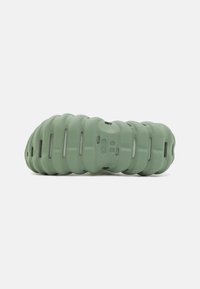 Green molded footwear featuring a ribbed design with ventilation holes and a textured surface, providing a lightweight and flexible structure.