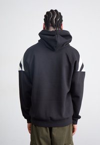 Svart hoodie med avslappnad passform, med en stor huva och vita accentlinjer på axlarna. Tillverkad av mjukt, texturerat material.