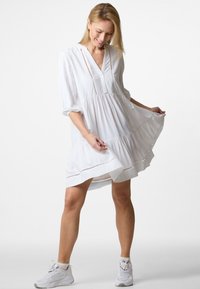 Weißes Kleid mit V-Ausschnitt, Dreiviertelärmeln und rüschigem Saum. Hat vertikale Streifen und dekorative Nähte entlang der Nähte.