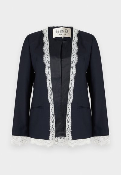 Μπλέιζερ ναυτικού με λευκή δαντέλα κατά μήκος του μπροστινού ανοίγματος, των μανσετών και του τελειώματος, χωρίς γιακά και με δύο μπροστινές τσέπες.