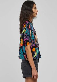 Blusa cropped a maniche corte con motivi floreali e astratti multicolori su sfondo nero; tessuto leggero con vestibilità rilassata.