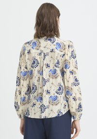 Florale Bluse in Creme mit blauen und braunen Mustern. Verfügt über lange Ärmel und eine lockere Passform, mit strukturierter Stoffqualität und Knopfdetails.