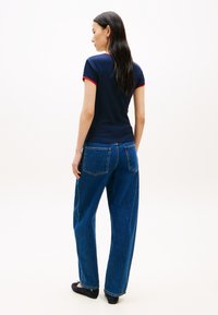 Μπλε σκούρο εφαρμοστό T-shirt με κόκκινη διακόσμηση, σε συνδυασμό με χαλαρό μπλε τζιν και μαύρες πλατφόρμες, που δείχνει μια casual πίσω όψη.