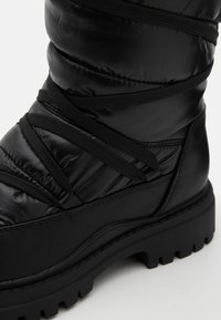 Black insulated boot with quilted puffer design, featuring a rubber sole, prominent laces, and a smooth, shiny texture.