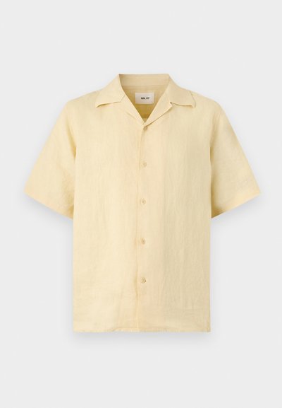Chemise en lin beige à manches courtes, boutonnée, avec un col cranté, présentée sur un fond clair.