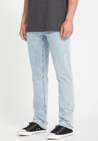 Lichtblauwe denim jeans met een rechte pasvorm, voorzien van subtiele whiskers en stikseldetails, gecombineerd met zwarte canvas sneakers.
