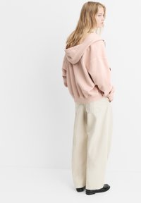 Roze oversized hoodie met een trekkoordcapuchon, gecombineerd met brede beige broek. De stof lijkt zacht, met subtiele stikseldetails.