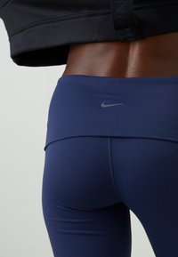 Gros plan d'une personne portant des leggings Nike bleu marine et un haut noir, montrant le bas du dos et la taille.