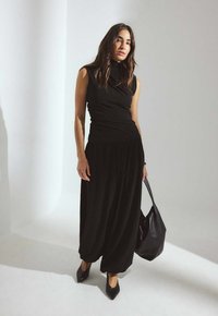 Musthave must рigneeta t-särgid, millel on vabalt langev kaelus, koos lahtiste mustade pükstega. Mudel hoiab musta kotti ja on jalas terava ninaga mustad kontsad.
