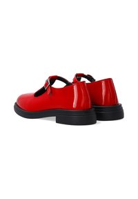 Red patent leather shoes with a rounded toe, adjustable buckle strap, and black rubber sole. Features a smooth texture and minimalist design.