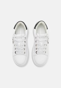 Weißer Sneaker mit einem glatten Leder-Obermaterial, schwarzen Lackleder-Details an der Ferse, strukturierter weißer Gummisohle und metallischen Ösen.