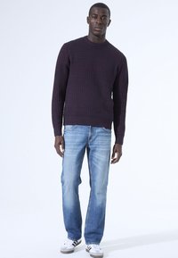 Gebreide marineblauwe trui met een gestructureerd patroon, ronde hals, gecombineerd met lichtblauwe jeans met rechte pijpen en witte sneakers met zwarte accenten.
