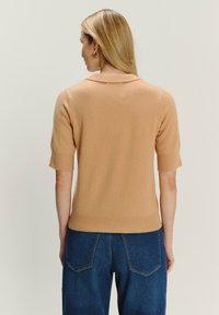Krátky rukáv, svetlohnedý pletený sveter s golierom, rebrovaným lemom a hladkou textúrou, skombinovaný s džínsami so stredným praním.