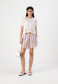 Balts adītais cropped tops, svītraini lavandas un zelta šorti, apvienoti ar mazu baltu rokassomu un gaišām, plakanu zoli apaviem.