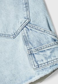 Gros plan d'un tissu en denim bleu clair montrant deux poches arrière superposées et des détails de couture visibles.