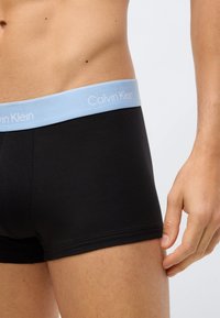 Juodos bokserio kelnaitės su šviesiai mėlynu elastingu juosmeniu, ant kurio yra "Calvin Klein" logotipas. Lygus audinys, prigludusi forma ir aiškiai apibrėžtas kojų atidarymas.