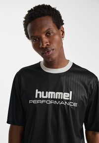 Black short-sleeve t-shirt with vertical stripes, white collar, featuring "hummel PERFORMANCE" logo in bold white letters on the front.