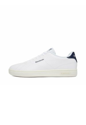 Hvid lav Reebok sneaker med navy hælflig, hvide snørebånd og beige sål, der viser sidevisning med mærkelogoer på siden og sålen.