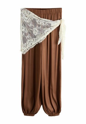 Brune bukser med vide ben med elastisk talje og manchetter, draperet med et hvidt blomsterblonde tørklæde bundet i siden.