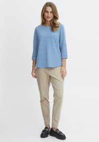 Blå og hvidt stribet bluse med trekvartærmer, parret med beige bukser og sorte loafers med guldfarvede hardware-detaljer.