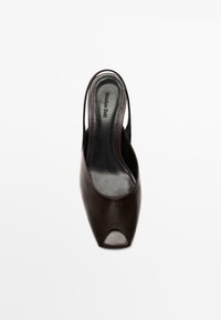Mules ouvertes en cuir marron avec une texture lisse, dotées de brides fines sur les côtés et d'une silhouette élégante et moderne.