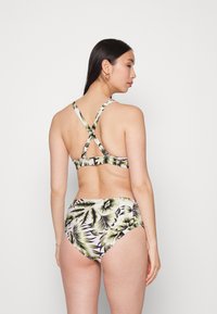 Biquíni em duas peças com um padrão floral que apresenta folhas verdes e pretas. O top tem alças cruzadas nas costas e um fecho, enquanto as partes de baixo são de cintura alta.