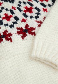 Sweter dziany w kremowym kolorze z czerwonymi i granatowymi geometrycznymi wzorami. Teksturowana tkanina z detalami prążkowanych mankietów.