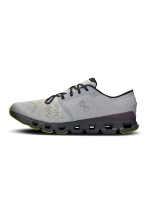 Chaussure de sport gris clair avec lacets noirs, semelle segmentée gris foncé, accents verts et dessus en mesh respirant, vue latérale.