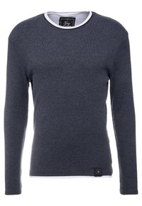 Dark gray long-sleeve crewneck sweater layered over a white undershirt with a visible tag at the collar and a small black label near the hem.
