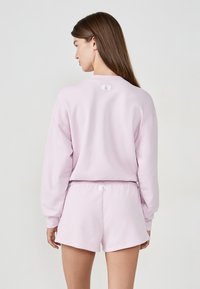 Jasnoróżowy, oversize'owy sweatshirt z długimi rękawami, w połączeniu z pasującymi szortami. Oba wykonane z miękkiego materiału, z metkami z tyłu.