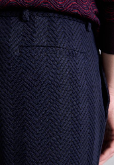 Námořnické modré kalhoty s vyvýšenou herringbone texturou, mají zadní kapsu a mají přiléhavý střih.