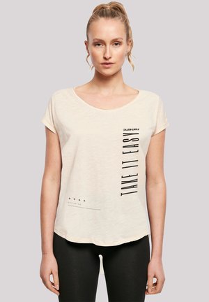 Light beige short-sleeve t-shirt with a rounded neckline, featuring black text and graphic elements on the front, and a relaxed fit.